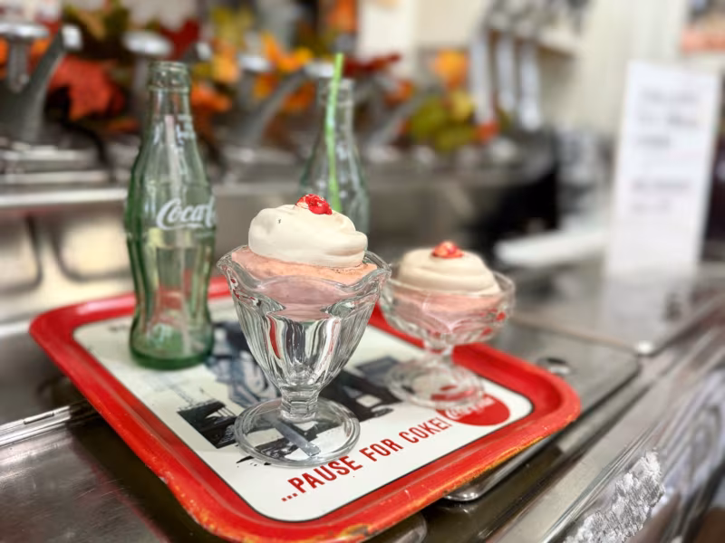 Ice cream sundaes in glass dishes and a Coca-Cola bottle on a red tray at the old soda fountain counter