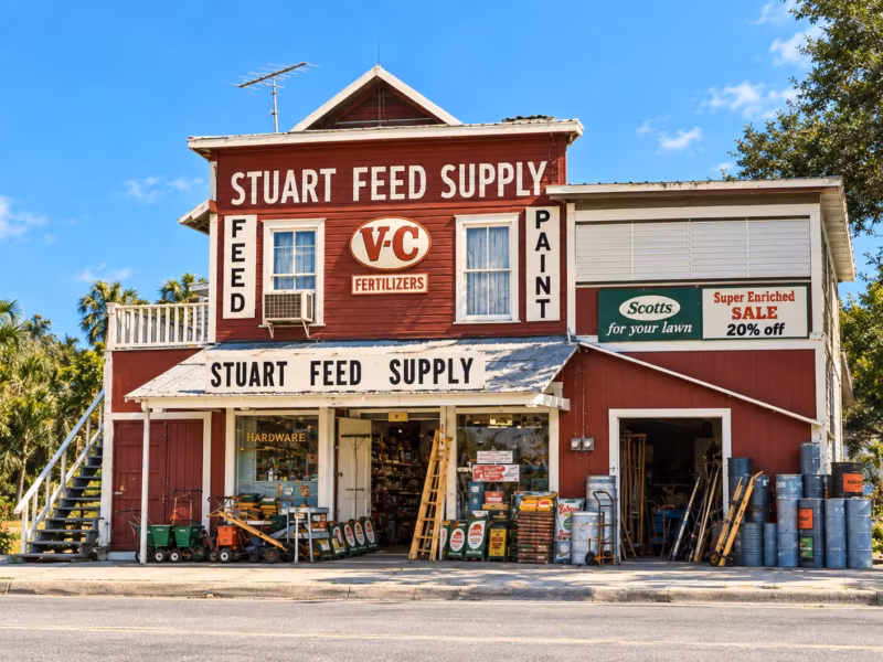 The red Stuart Feed Supply building with feed and paint signs and goods stacked out front, in the mid-1980s
