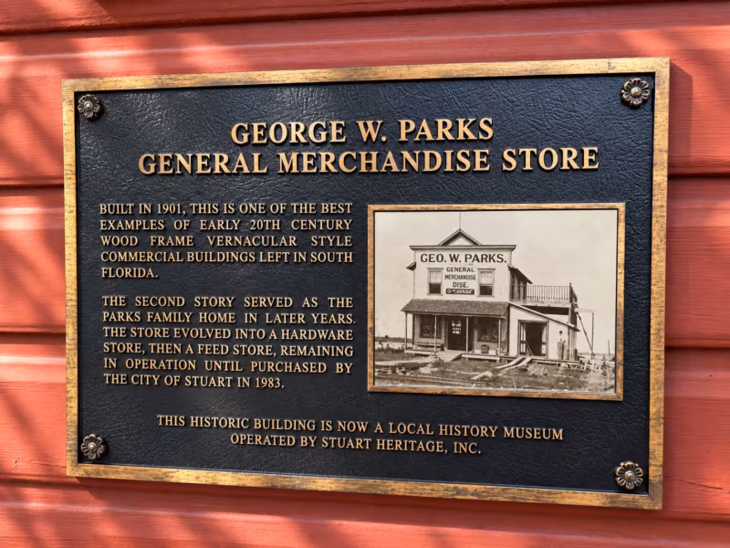 Bronze plaque on the red siding reading George W. Parks General Merchandise Store, with an early photo of the store